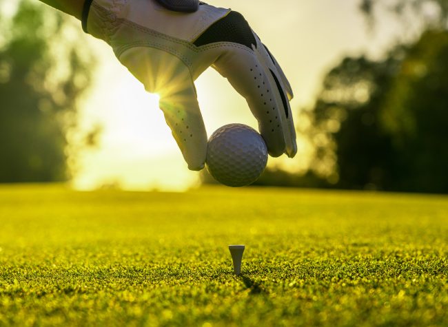 Closeup of golfer wearing glove placing golf ball on tee at golf course
